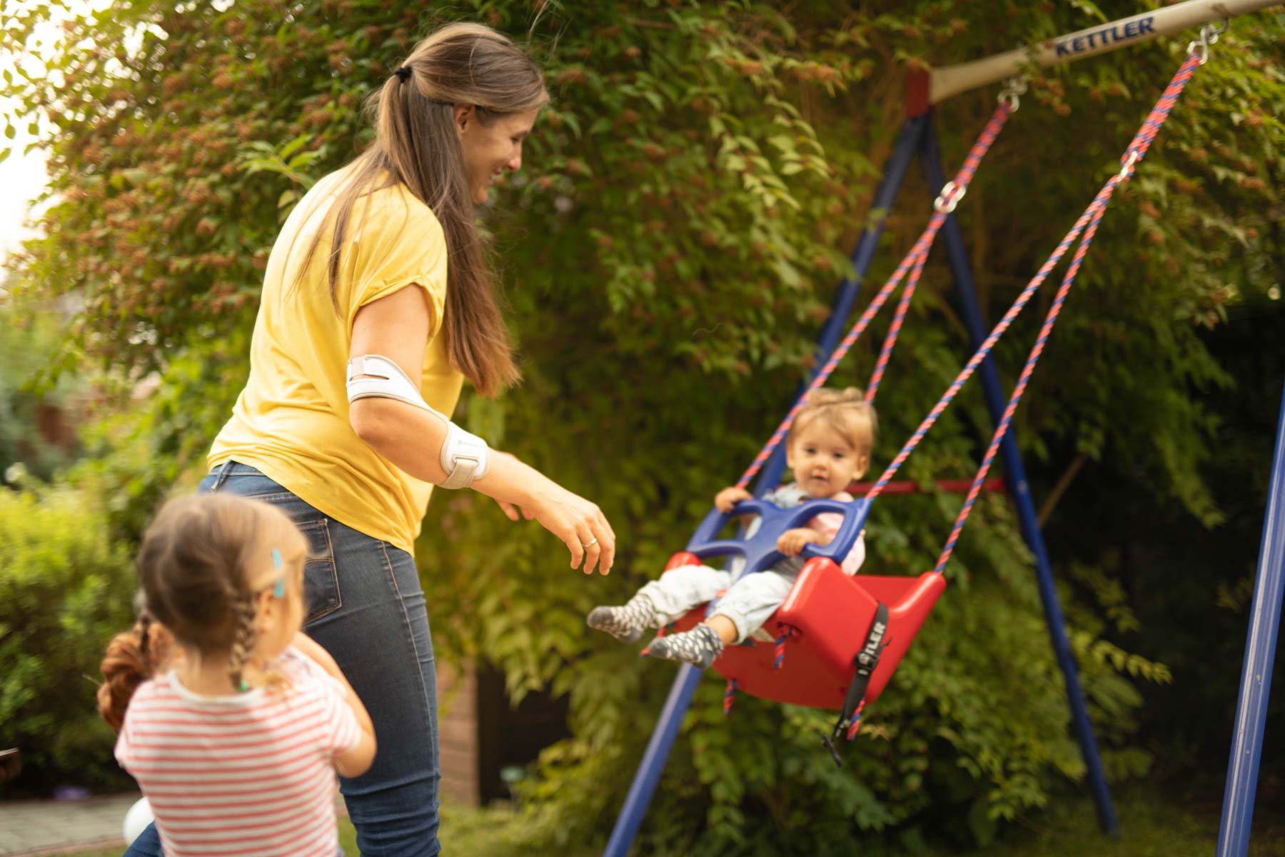 Mother with two children rocks her offspring while wearing Masalo cuff against tennis elbow, golfer's elbow, mouse elbow