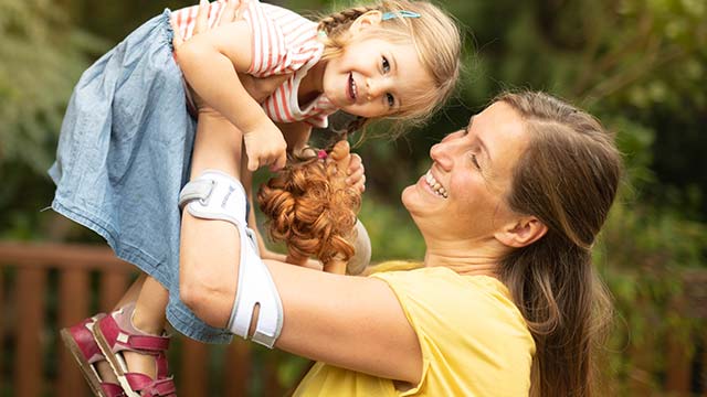 Woman lifts little girl in the air while wearing the Masalo cuff for tennis elbow with the unique counter-traction principle of action for epicondylitis